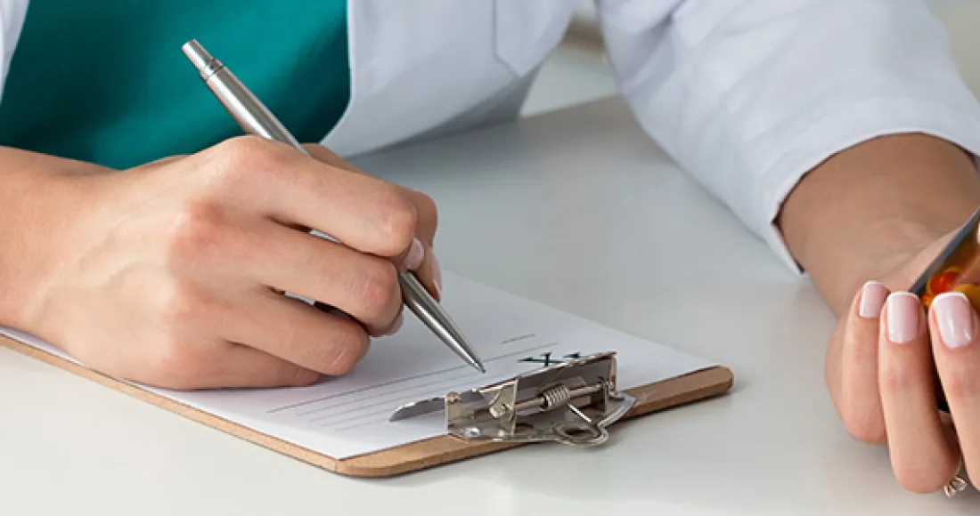 Doctor writing on prescription pad, holding pill bottle.