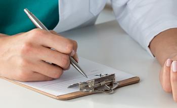 Doctor writing on prescription pad, holding pill bottle.